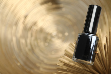 Stylish presentation of black nail polish in bottle on golden textured surface, closeup. Space for textの写真素材