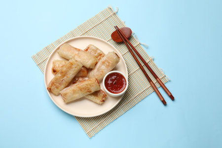 Fried spring rolls and sauce served on light blue table, top view