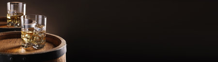 Whiskey with ice cubes in glasses on wooden barrels against dark background, space for text. Banner designの写真素材