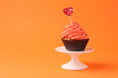Delicious cupcake with bright cream and heart topper on orange background. Space for textの写真素材