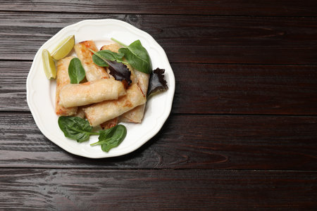 Plate with tasty fried spring rolls, spinach and lime on wooden table, top view. Space for text