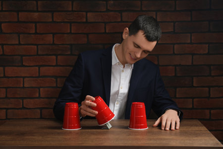 Shell game. Man showing dollar banknote under cup at wooden tableの写真素材