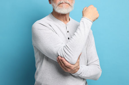 Arthritis symptoms. Man suffering from pain in elbow on light blue background, closeupの写真素材