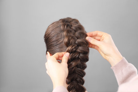 Professional stylist braiding woman's hair on gray background, closeupの写真素材