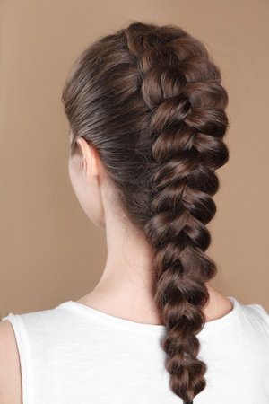 Woman with braided hair on light brown background, back view