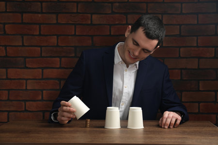 Shell game. Man showing stack of coins under cup at wooden tableの写真素材
