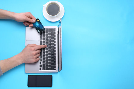 Online payment. Man with laptop, credit card, smartphone and coffee on light blue background, top view. Space for textの写真素材