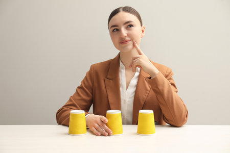 Thoughtful woman playing shell game at white tableの写真素材