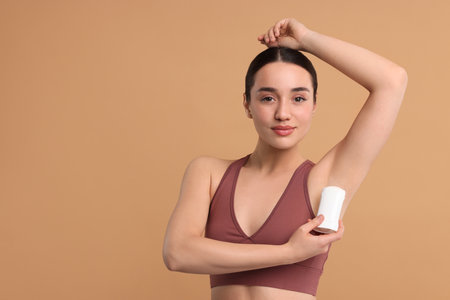 Beautiful woman applying deodorant on beige background, space for textの写真素材