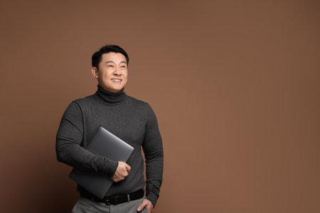 Portrait of happy man with laptop on brown background. Space for textの写真素材