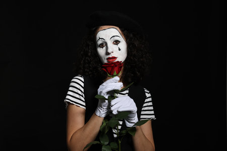 Young woman in mime costume with red rose posing on black backgroundの写真素材