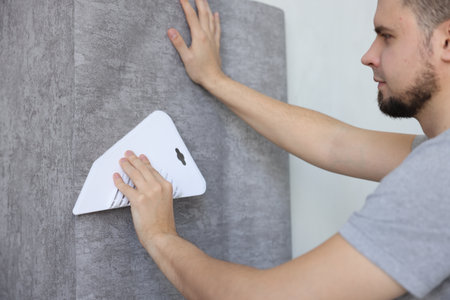 Man smoothing stylish gray wallpaper in roomの写真素材