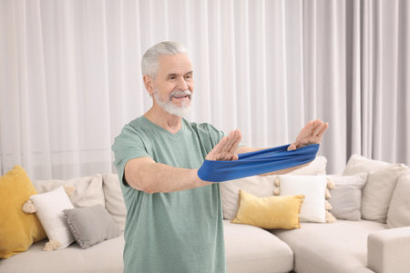 Senior man doing exercise with fitness elastic band at homeの写真素材