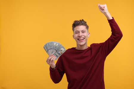 Happy man with dollar banknotes on yellow background. Space for textの写真素材