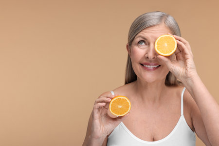 Beautiful woman with halves of orange rich in vitamin C on beige background, space for textの写真素材