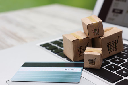 Internet store. Small cardboard boxes with shopping carts, credit card and laptop on table, closeup....