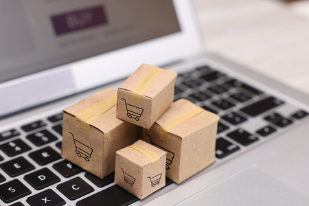 Internet store. Small cardboard boxes with shopping cards on laptop, closeup