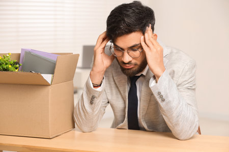 Unemployment problem. Frustrated man with box of personal belongings at desk in officeの写真素材