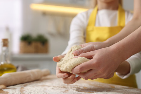Making bread. Mother and her daughter kneading dough at wooden table in kitchen, closeupの写真素材