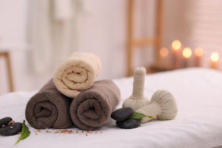 Spa stones, rolled towels and herbal bags on massage table indoorsの写真素材