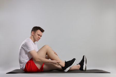 Man suffering from leg pain on mat against gray background
