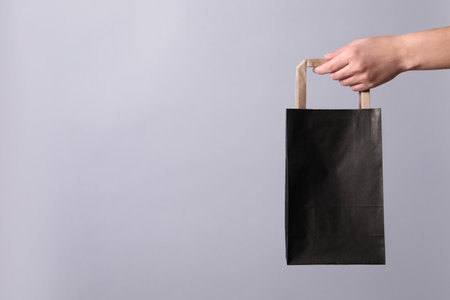 Woman holding paper shopping bag on gray background, closeup. Space for textの写真素材