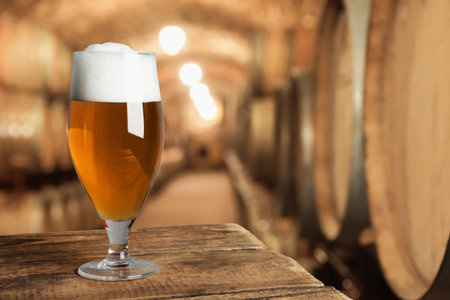 Glass with fresh beer on wooden table in cellar, space for textの写真素材
