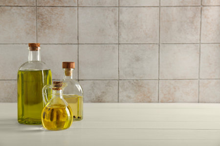 Vegetable fats. Different oils in glass bottles on white wooden table against tiled wall, space for textの写真素材