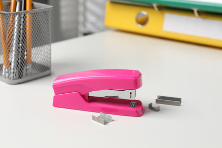 Stapler and metal staples on white table indoors