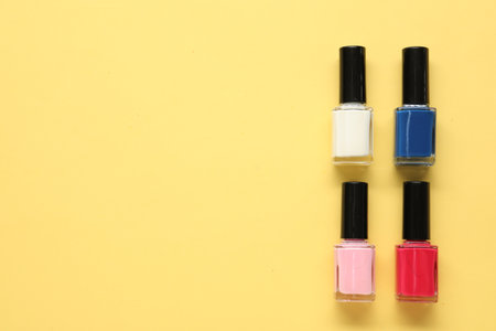 Bright nail polishes in bottles on yellow background, flat lay. Space for textの写真素材