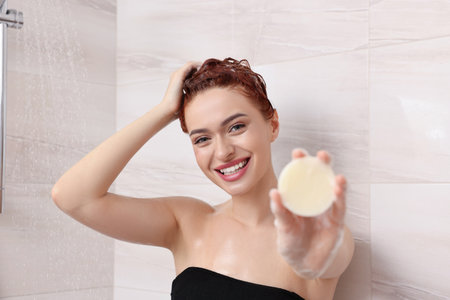 Happy young woman with solid shampoo bar in showerの写真素材