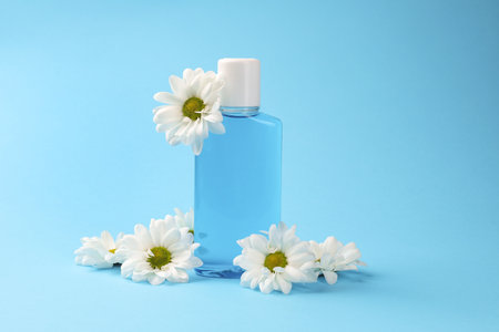 Fresh mouthwash in bottle and flowers on light blue backgroundの写真素材