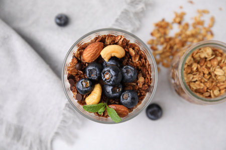 Tasty granola with berries, nuts and mint in glass on light table, top view