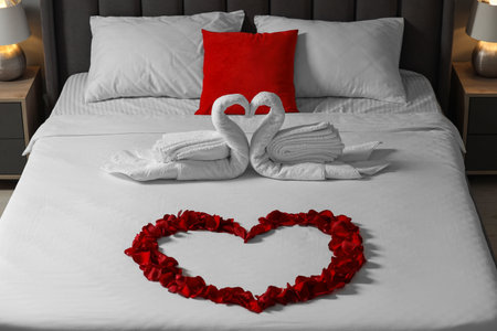Honeymoon. Swans made with towels and heart of beautiful rose petals on bed in roomの写真素材