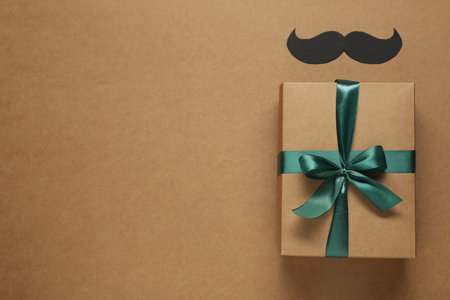 Gift box and paper mustache on brown background, flat lay with space for text. Father's day celebrationの写真素材