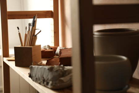 Set of different crafting tools and clay dishes on wooden rack in workshopの写真素材