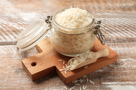Raw basmati rice in glass jar and scoop on wooden tableの写真素材