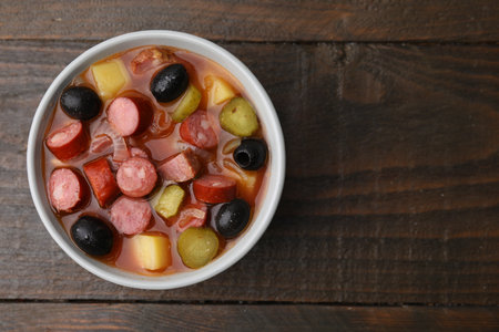 Meat Solyanka soup with thin dry smoked sausages in bowl on wooden table, top view. Space for textの写真素材