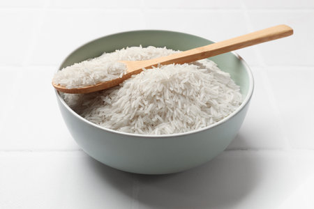 Raw basmati rice in bowl and spoon on white tiled tableの写真素材