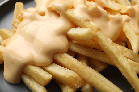 Delicious French fries with cheese sauce on plate, closeup
