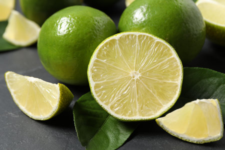 Fresh ripe limes and leaves on black table, closeupの写真素材