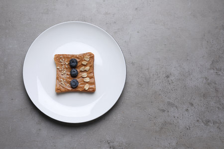 Toast with tasty nut butter, blueberries and nuts on gray textured table, top view. Space for textの写真素材