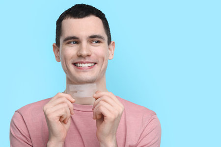 Young man with whitening strips on light blue background. Space for textの写真素材