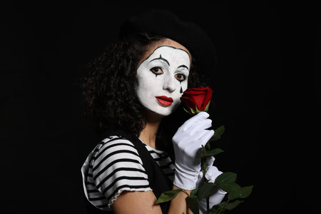 Young woman in mime costume with red rose posing on black backgroundの写真素材