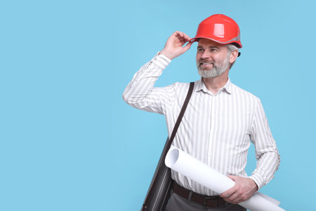 Architect in hard hat holding draft on light blue background. Space for textの写真素材