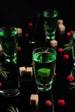 Absinthe in shot glasses, cranberries, rosemary and brown sugar on mirror table. Alcoholic drink