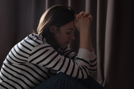 Sad young woman near closed curtains indoorsの写真素材