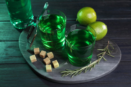 Absinthe in glasses, rosemary, brown sugar and lime on wooden table. Alcoholic drink