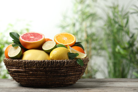Different fresh citrus fruits and leaves in wicker basket on wooden table against blurred background, closeup. Space for textの写真素材