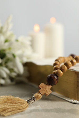Bible, rosary beads and church candles on light table, closeup